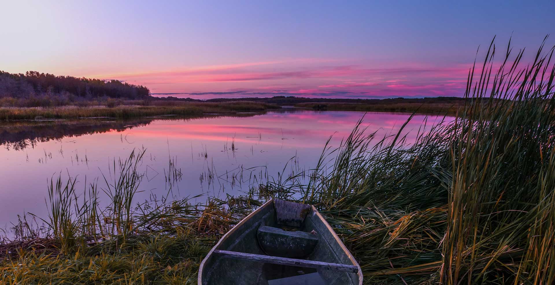 sunset image of a canoe sitting in the reeds along the Saskatchewan Riverbank