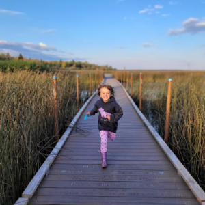Young girl running toward the camera along the boardwalk on a fall evening