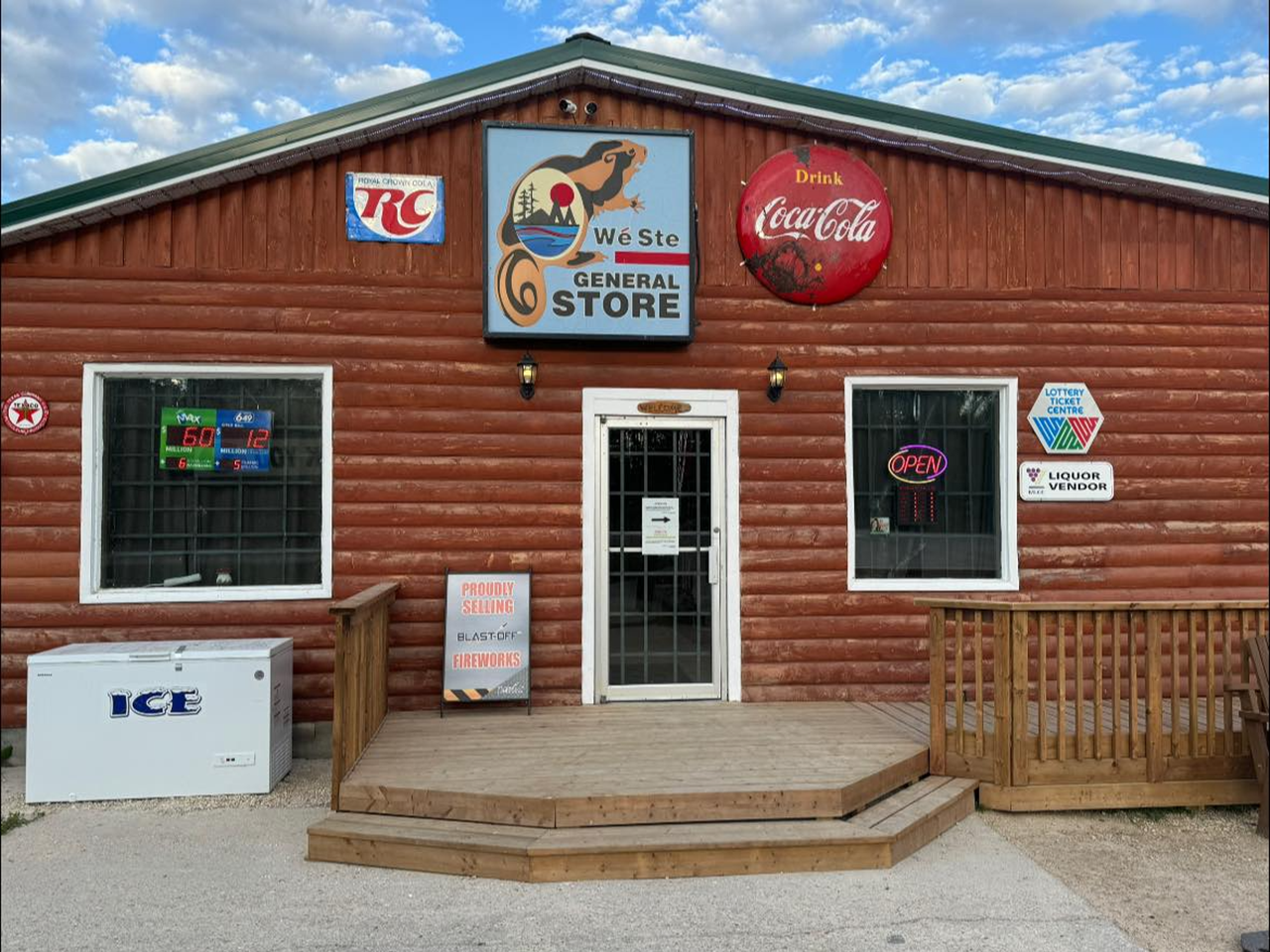 Wood siding Wanless General store with the vintage Wé Ste General Store sign, CocaCola and Royal Crown Cola RC signs. They have a small deck in front and other signs surrounding the two large windows.