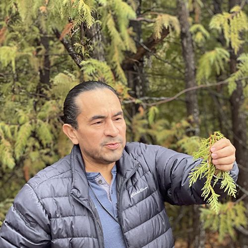Shwerin Moore teaching youth about picking medicine, holding up some cedar